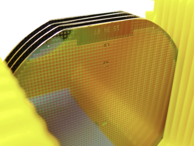 Mehrere gestapelte Halbleiter-Wafer in einer Transportbox, mit reflektierenden Oberflächen und feinen strukturellen Details.